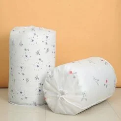 2 white color round storage bags for blankets and quilts are kept besides each other on the floor fully packed with clothes