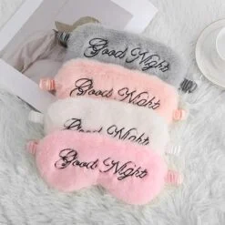 Plush eye mask is kept on a plush mat in pink, white, orange, and grey color