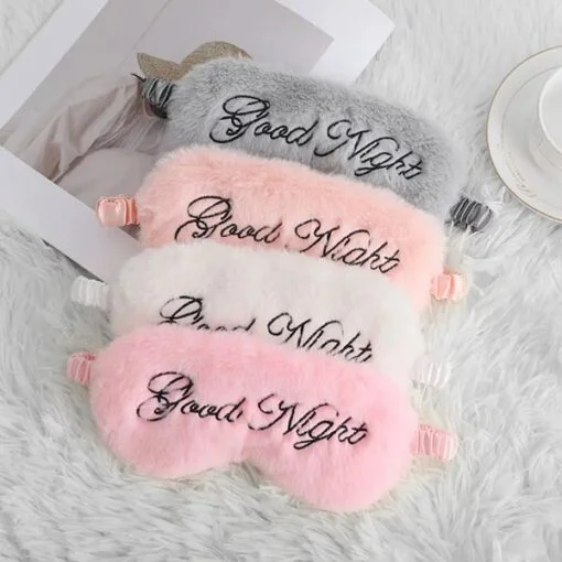 Plush eye mask is kept on a plush mat in pink, white, orange, and grey color.