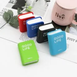 Diary shape contact lens case with mirror is shown in green, sky blue, black, blue, and red color besides a coffee mug on a news paper