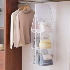 All purses are organized in a white color purse hanging organizer besides 2 tops in a wardrobe space.