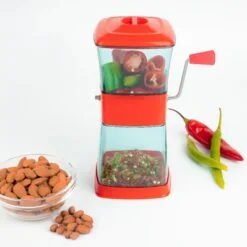 Double layer red color big vegetable chopper is placed besides almonds bowl and chilies.