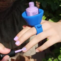 A woman is applying nail paint using blue color wearable nail polish holder.