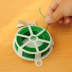 A person is using white color plastic twist tie wire to tie green color wire.
