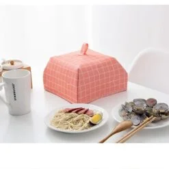 Foldable insulated food cover is used on a dining table besides dishes and a cup