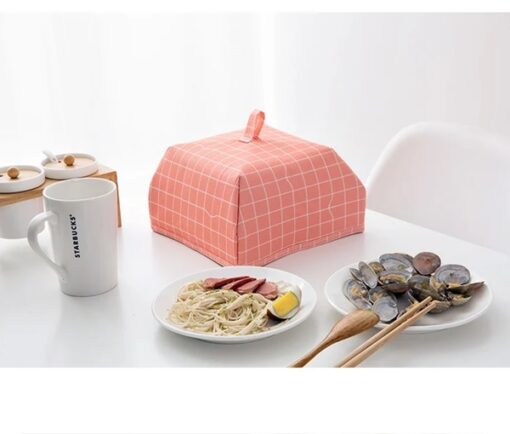 Foldable insulated food cover is used on a dining table besides dishes and a cup.