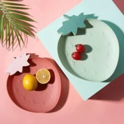 Half cutted lemons are placed in a pink color strawberry shaped plate. 2 Cherries are placed in a blue color strawberry shaped plate