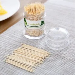 Wooden tooth pick set is placed on a dining table along with a bottle filled with wooden tooth pick.