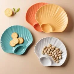 Blue color shell shape plastic snack plate is used for biscuits and white one used for pistachios. Orange and mustard yellow are kept empty.