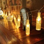 A strand of 16-LED Mini Glass Bottle String Light draped across a fence, casting a warm and inviting glow. Some bottles are filled with small fairy lights for an extra touch of magic.