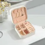 Portable Mini Travel Jewelry Box A luxurious, compact Portable Mini Travel Jewelry Box crafted from PU leather. It rests on a nightstand, with the lid open showcasing various compartments and velvet lining for storing jewelry.