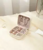 A luxurious, compact Portable Mini Travel Jewelry Box crafted from PU leather. It rests on a nightstand, with the lid open showcasing various compartments and velvet lining for storing jewelry.