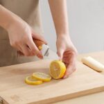 The 2-in-1 peeler and knife being used to slice a tomato, showcasing the serrated blade handling the tough skin with ease. (