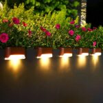 A set of four LED Solar Deck Lights with sleek designs, mounted on a wooden deck, illuminating the surrounding area at night.