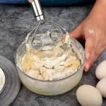 A person using the dough whisk mixer to incorporate ingredients in a mixing bowl.