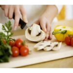 A person chopping vegetables on the chopping board, using one of the knives from the set. (