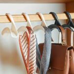 A chrome-plated multifunctional bag hanger displayed on a closet rod, holding a tote bag. Person hanging a backpack on a multifunctional bag hanger attached to a wall hook. Stack of multifunctional bag hangers in various colors (depending on availability) on a shelf.