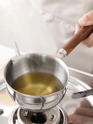 The stainless steel mini saucepan on a stovetop, with a small amount of liquid simmering inside.